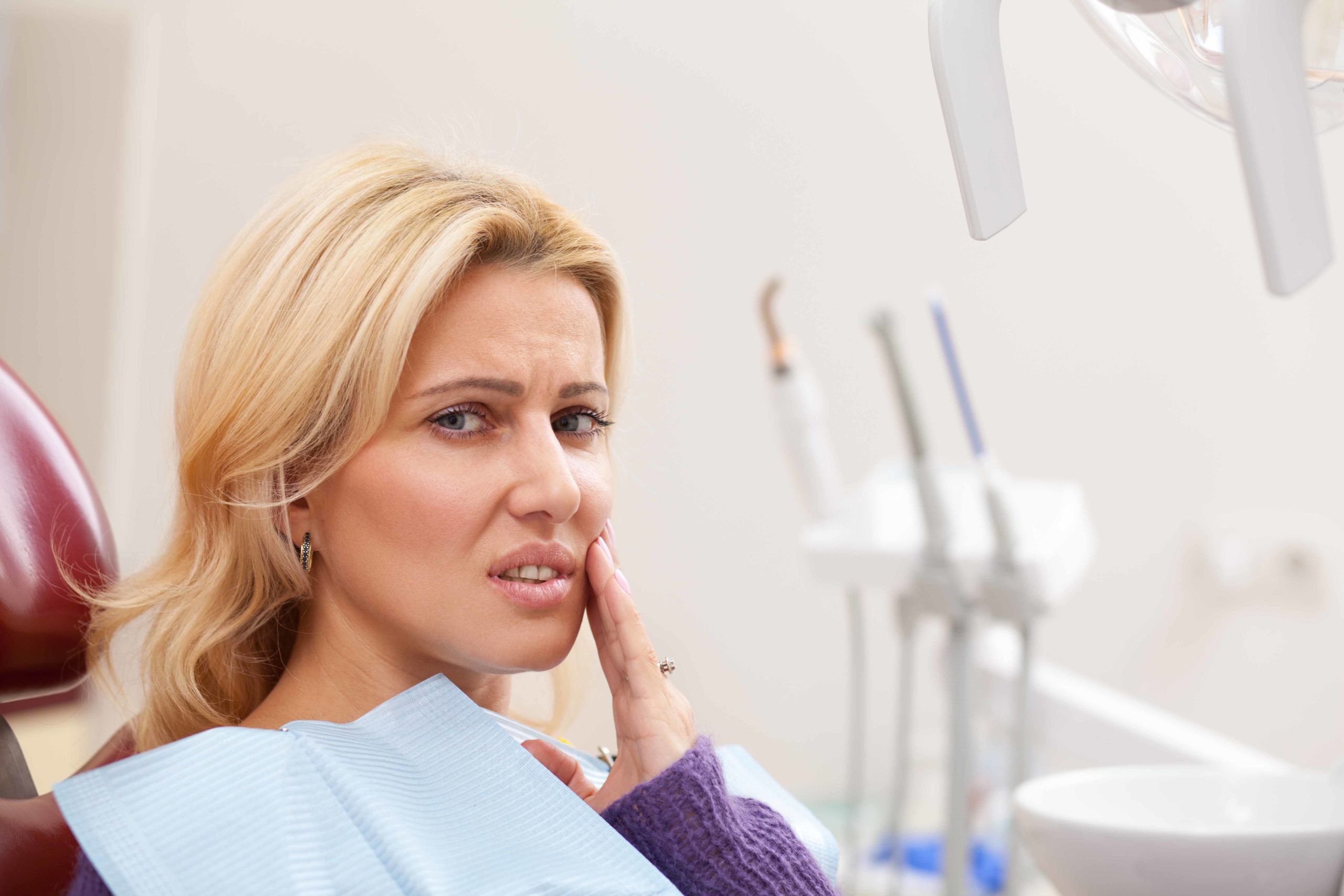 歯科の椅子に座っている女性が口元に手を当てて険しい顔をしている