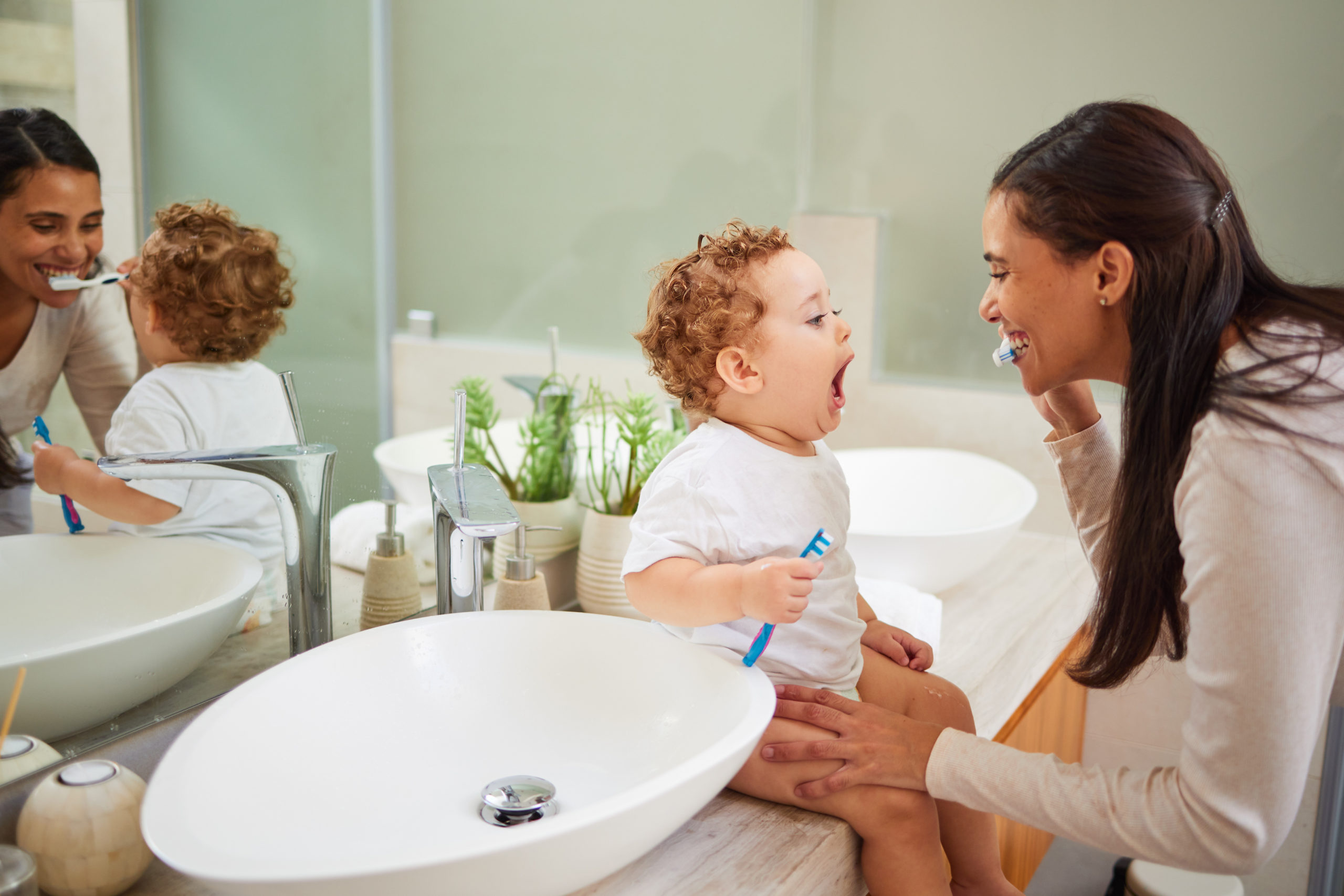 洗面台に赤ちゃんを座らせて歯磨きの仕方を教える母親