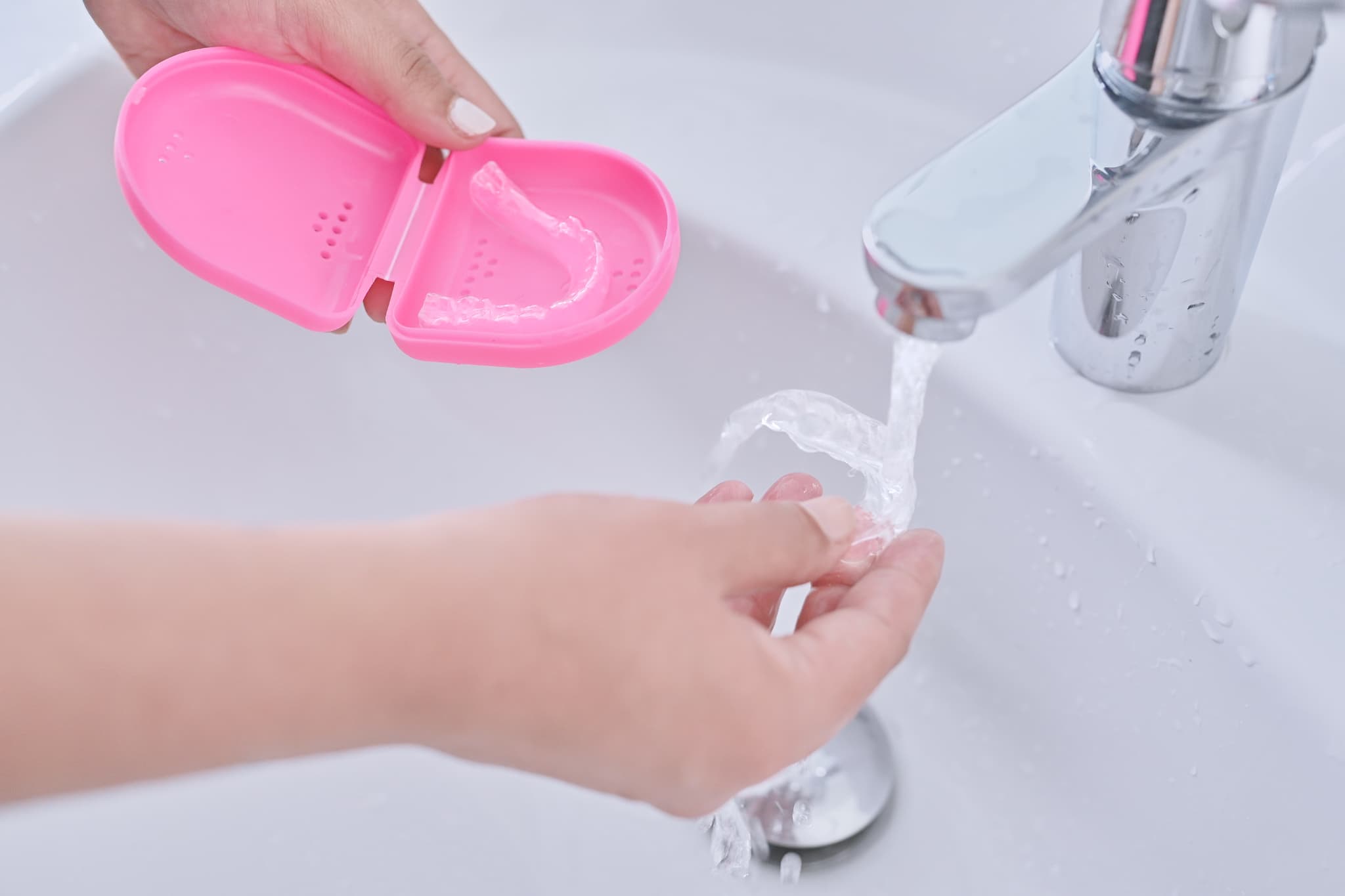 インビザラインのマウスピースを水で洗う女性