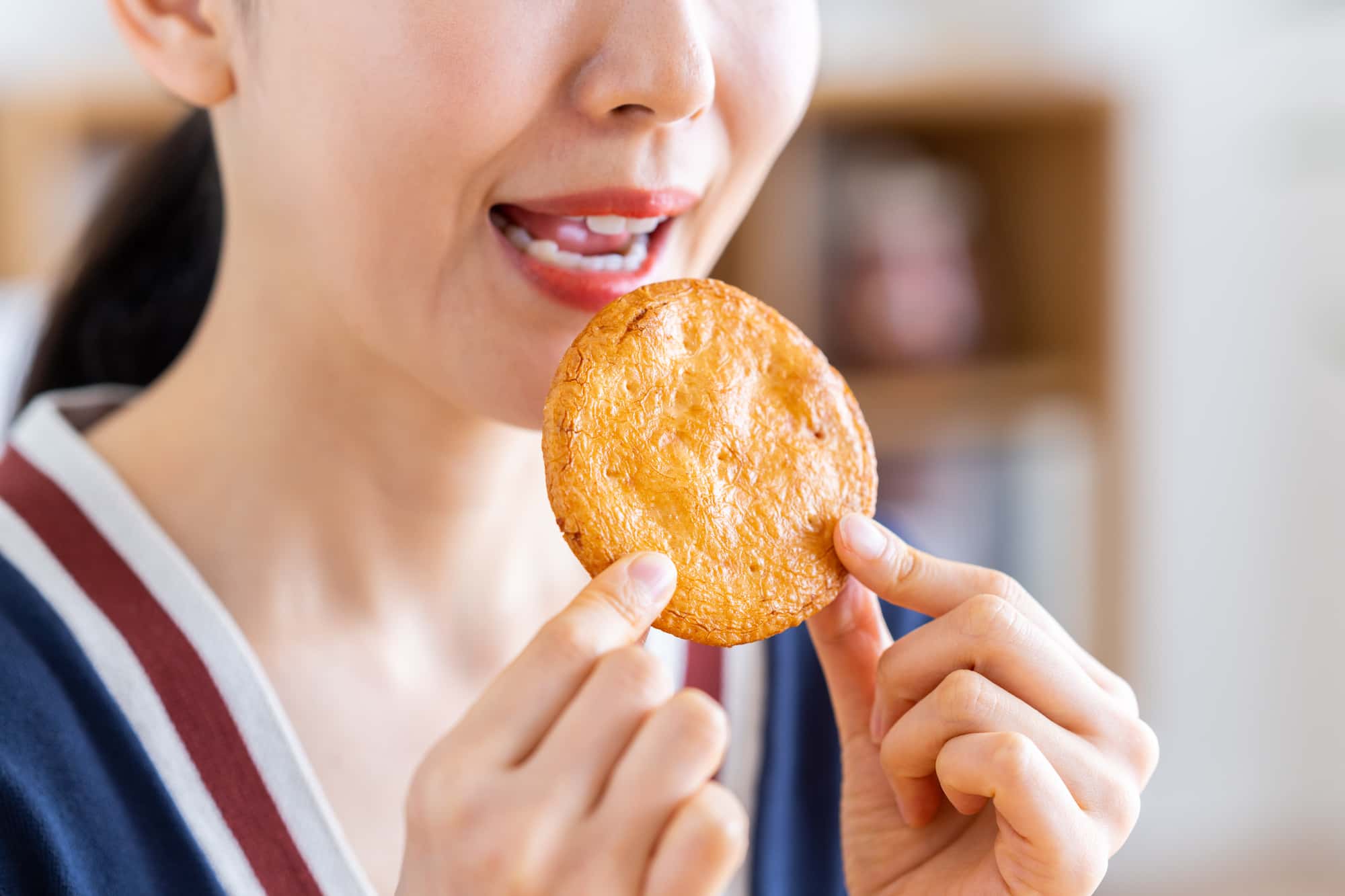 セラミックの歯が取れる原因になる固いせんべいを食べる女性